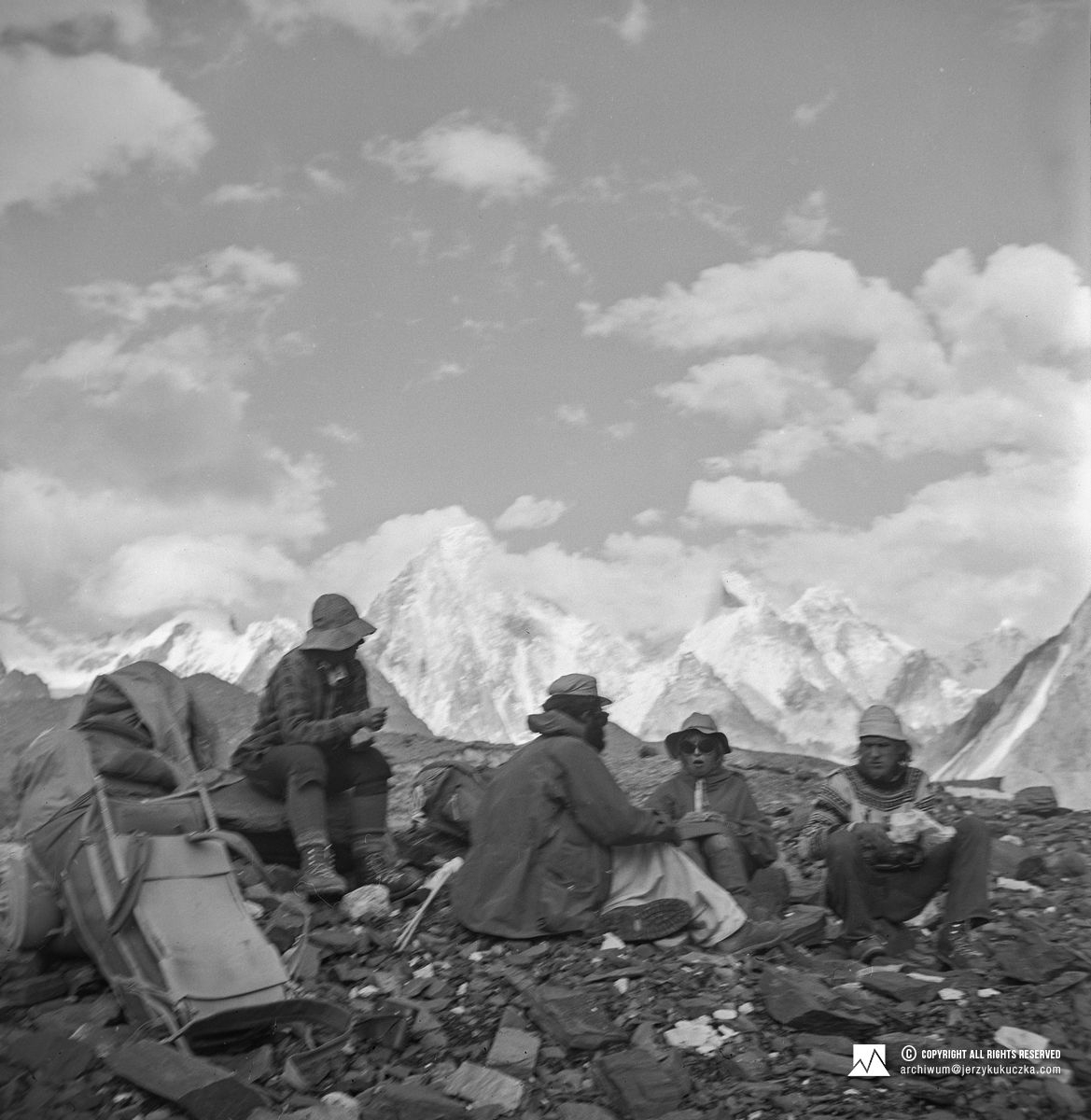 Biwak podczas powrotu z wyprawy. Od prawej: Andrzej Łapiński, Krystyna Palmowska, Władysław Leszek Woźniak i NN. W tle masyw Gasherbrum z Gasherbrumem IV w centrum (7925 m n.p.m.).